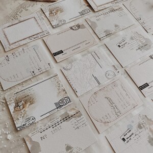 May include: A collection of vintage-style postcards with distressed edges and faded ink. The postcards feature various designs, including a map, a compass, and a stamp with the words "By Air Mail".