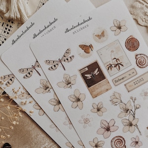 May include: Three sheets of stickers featuring illustrations of butterflies, flowers, and other nature-inspired designs. The stickers are printed on white paper with a brown background. The text "albumlovehandmade stickers" is printed on each sheet.