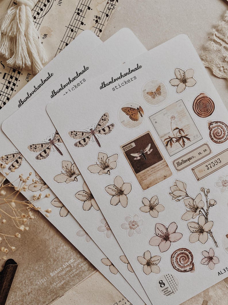 May include: Three sheets of stickers featuring illustrations of butterflies, flowers, and other nature-inspired designs. The stickers are printed on white paper with a brown background. The text "albumlovehandmade stickers" is printed on each sheet.
