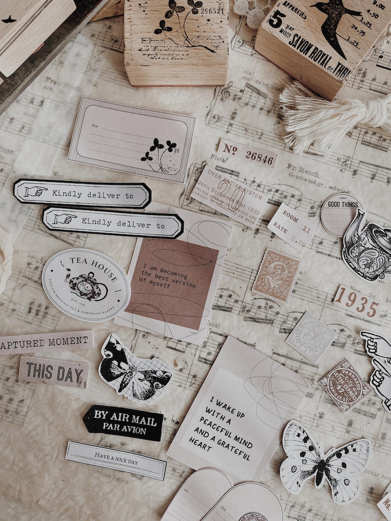 May include: A collection of vintage-style paper ephemera with a tea house theme. The ephemera includes stamps, stickers, and paper scraps with images of butterflies, teacups, and flowers. The text on the ephemera includes phrases like "Tea House", "By Air Mail", "I Wake Up With A Peaceful Mind", and "Captured Moment".