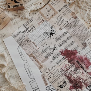 May include: A collection of vintage ephemera, including a sheet of music, a stamp with a witch on a broom, a piece of lace, and several paper tags with text and images. The tags feature butterflies, a clock, and a red ink stain. The text on the tags includes "Collect Moments", "This Moment", "Destination", and "Captured Moment".