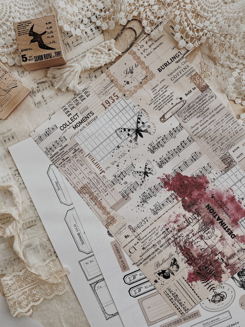 May include: A collection of vintage ephemera, including a sheet of music, a stamp with a witch on a broom, a piece of lace, and several paper tags with text and images. The tags feature butterflies, a clock, and a red ink stain. The text on the tags includes "Collect Moments", "This Moment", "Destination", and "Captured Moment".