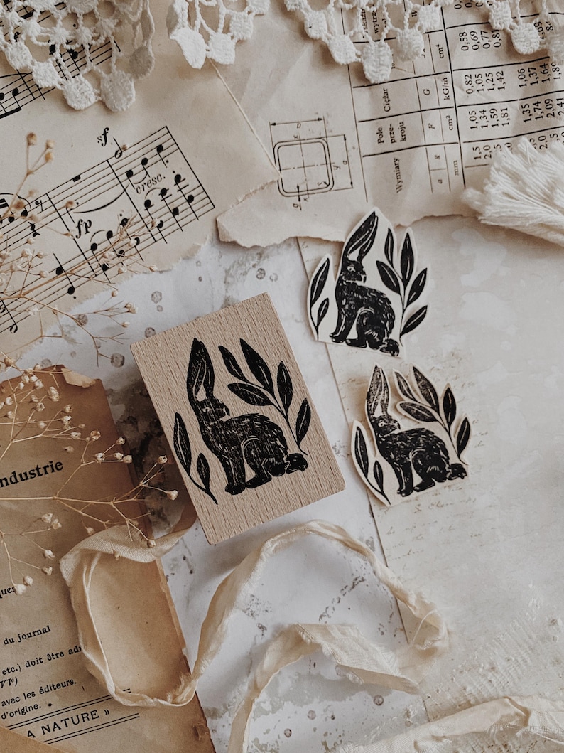 May include: A rectangular wooden rubber stamp and two die-cut paper stickers, each featuring a black ink illustration of a rabbit surrounded by leaves. The stamp has a light wood grain finish, while the stickers are off-white with black ink.