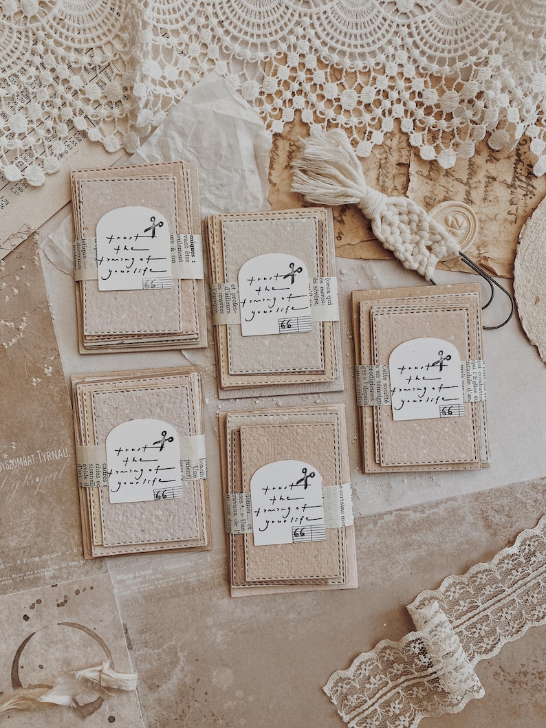 May include: A collection of handmade paper cards with stitched edges and a decorative paper band. Each card features the text "toast the turning of your life" and a musical note graphic. The cards are beige and cream colored.