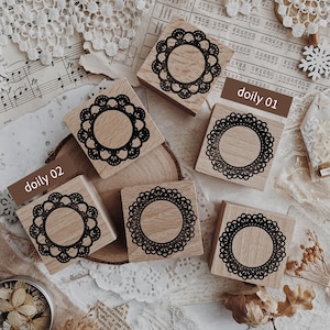 May include: Five square wooden stamps featuring intricate black circular lace doily patterns on the top surface. Two of the stamps are labeled with the text doily 01 and doily 02. The stamps have a light wood grain finish and a smooth texture.