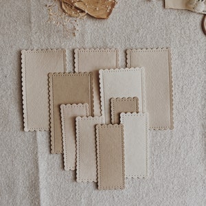 Puede incluir: Un conjunto de tarjetas rectangulares con bordes festoneados en tonos beige y marr&oacute;n claro, dispuestas sobre una superficie de lino neutra. Las tarjetas presentan un borde cosido. Las diferentes tama&ntilde;os de las tarjetas sugieren un estilo vintage o artesanal.