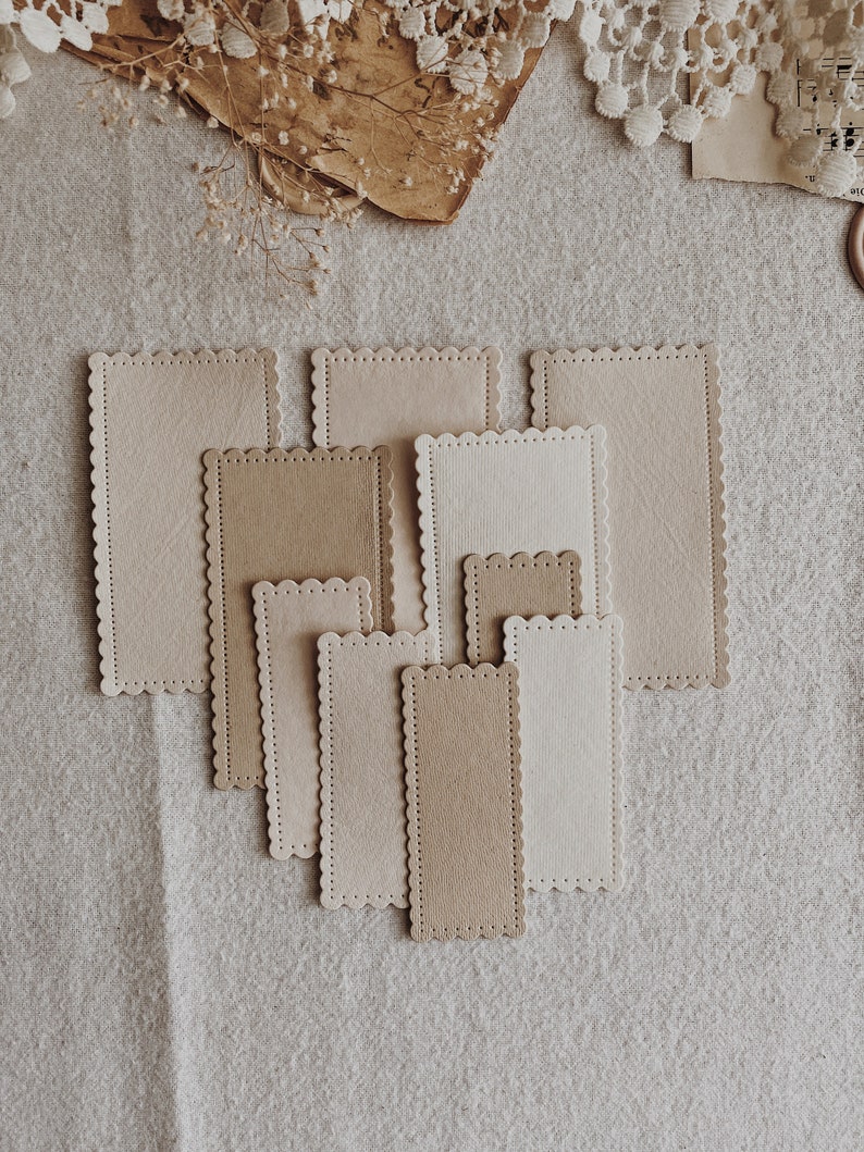 Puede incluir: Un conjunto de tarjetas rectangulares con bordes festoneados en tonos beige y marr&oacute;n claro, dispuestas sobre una superficie de lino neutra. Las tarjetas presentan un borde cosido. Las diferentes tama&ntilde;os de las tarjetas sugieren un estilo vintage o artesanal.