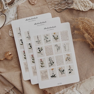 May include: Three sticker sheets with floral designs and the text "albumlovehandmade stickers." Each sticker features botanical illustrations resembling postage stamps. The background includes lace, fabric, and decorative tape.