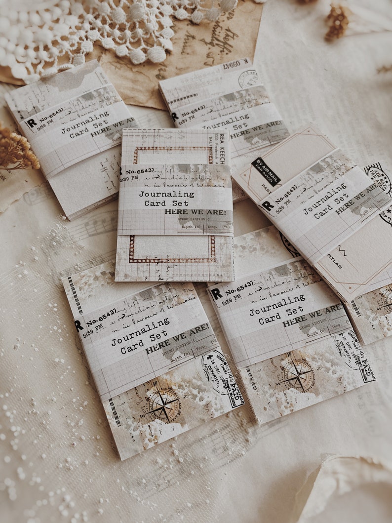 May include: Five vintage-style journaling card sets with a distressed white background and black text. Each card set has a label that reads "Journaling Card Set" and "Here We Are!" with a vintage stamp and a compass design.
