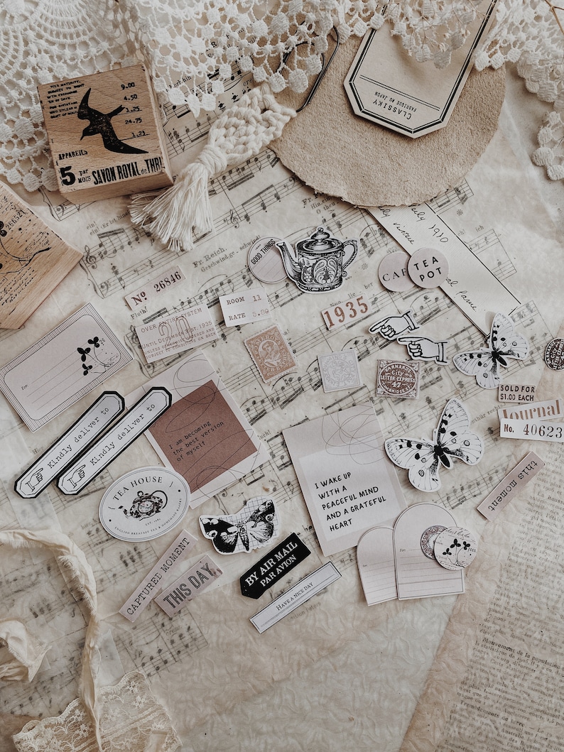 May include: A collection of vintage-style stickers and ephemera featuring butterflies, teapots, and other whimsical designs. The stickers are printed on white paper with black ink and have a distressed, aged look. The ephemera includes a small piece of music sheet, a vintage postcard, and a small piece of lace.