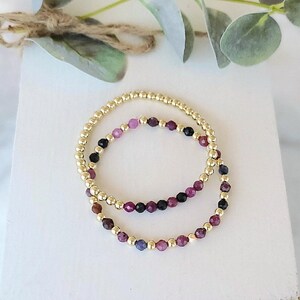 May include: Two gold bracelets with purple, pink, and black gemstone beads.