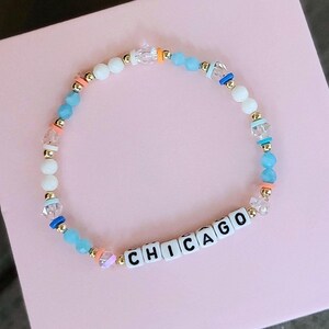 May include: A white, blue, and orange beaded bracelet with the word "CHICAGO" spelled out in black letters on white beads.