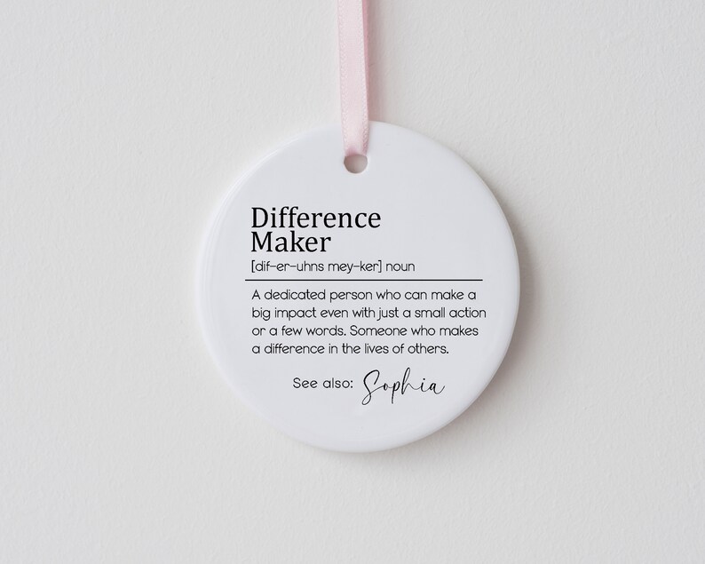 Op de afbeelding: Ronde witte ornament met zwarte tekst die luidt: "Difference Maker [dif-er-uhns mey-ker] noun Een toegewijde persoon die zelfs met een kleine actie of een paar woorden een grote impact kan hebben. Iemand die een verschil maakt in het leven van anderen. Zie ook: Sophia"