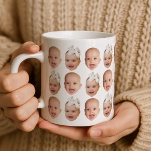 May include: A white ceramic mug featuring a repeating pattern of a baby's face. The baby has a light complexion, is smiling with an open mouth, and wears a large white hair bow. The mug has a curved handle on the left side for easy gripping.
