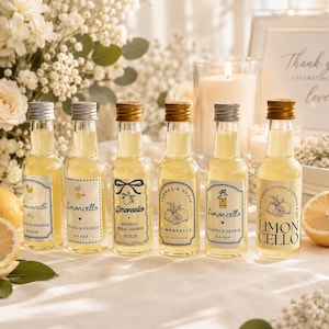 May include: Six small glass bottles filled with yellow limoncello, each featuring a unique custom label with lemon illustrations, names, and dates. The bottles have metallic screw caps in silver or gold and are arranged in a row on a white surface.