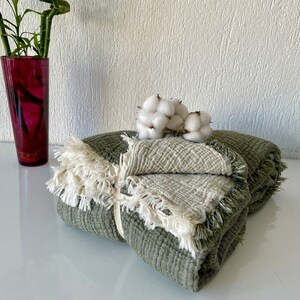 May include: A green and white waffle weave throw blanket with fringe trim. The blanket is folded and tied with a white ribbon. Cotton bolls are placed on top of the blanket.