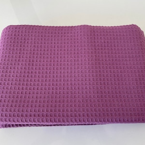 May include: A purple waffle weave throw blanket. The blanket is folded in half and is lying on a white surface.
