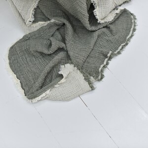 May include: A soft, green and white throw blanket with a fringed edge. The blanket is made of a waffle weave fabric and is folded on a white wooden floor.