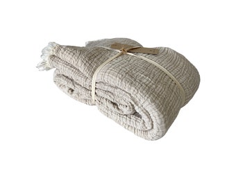 May include: A beige waffle weave throw blanket folded and tied with a brown ribbon. The blanket has a fringed edge.