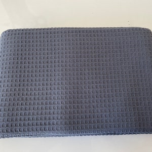 Peut inclure: Une couverture en tissu gaufré de couleur gris foncé. La couverture est pliée et posée à plat sur une surface blanche.