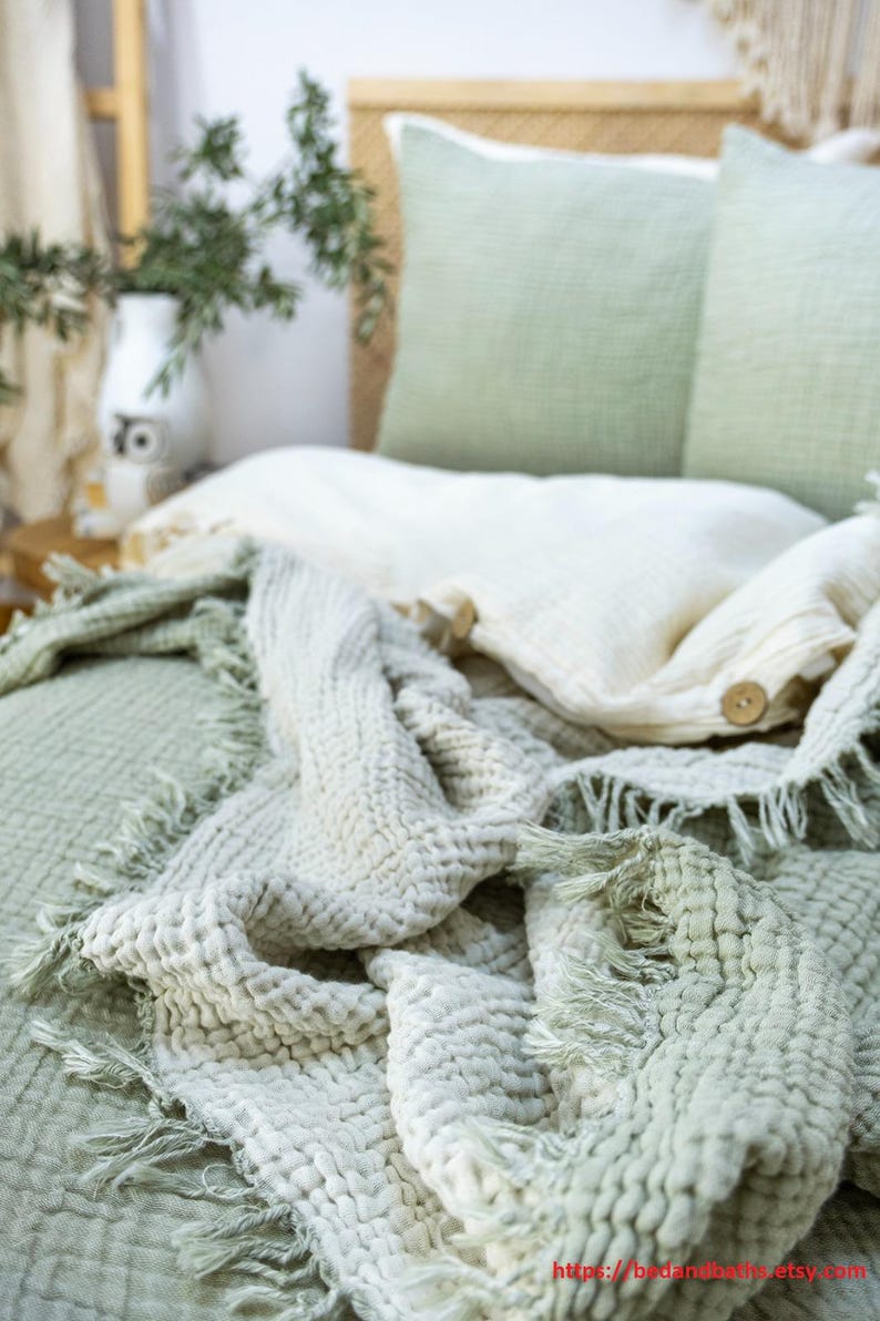 May include: A soft, textured throw blanket in a light green and white color scheme. The blanket has a fringed edge and is folded on a bed with matching pillows.
