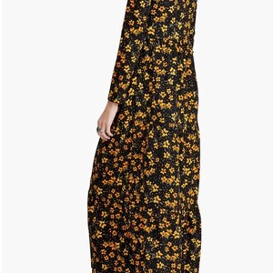 May include: A long-sleeved black dress with a yellow floral pattern. The dress has a V-neck and a tiered skirt. The model is wearing brown ankle boots with a block heel. The dress is made of a lightweight fabric.