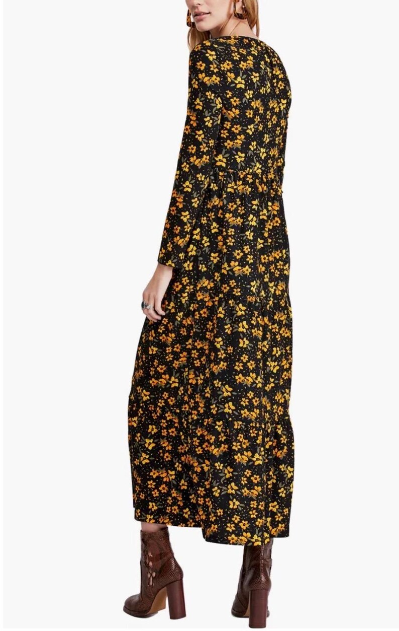 May include: A long-sleeved black dress with a yellow floral pattern. The dress has a V-neck and a tiered skirt. The model is wearing brown ankle boots with a block heel. The dress is made of a lightweight fabric.