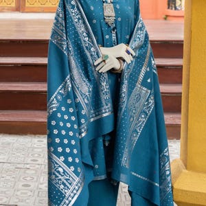 May include: A teal blue shalwar kameez with silver embroidery and a matching dupatta. The outfit features a floral pattern and a tassel on the dupatta.