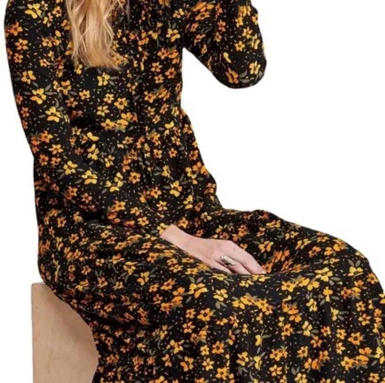 May include: Black long-sleeve dress with a yellow floral pattern. The dress has a high neckline and a flowing skirt. The floral print is composed of small, yellow flowers with green leaves. The dress appears to be made of a lightweight fabric.