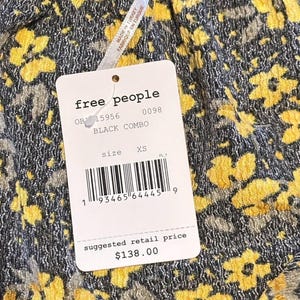 May include: A tag from Free People, with the text "BLACK COMBO" and "XS" size. The tag is attached to a garment with a yellow floral pattern on a black background. The suggested retail price is $138.00.