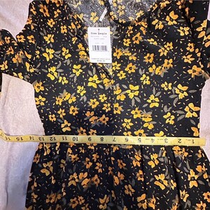 May include: Black dress with a yellow floral pattern. The dress has long sleeves and a collared neckline. A measuring tape is placed across the waist. The tag reads "free people".