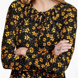 May include: Black long-sleeve dress with a yellow floral pattern. The dress features a tie-neck detail and a fitted waist. The fabric has a textured appearance. The dress is suitable for various occasions.