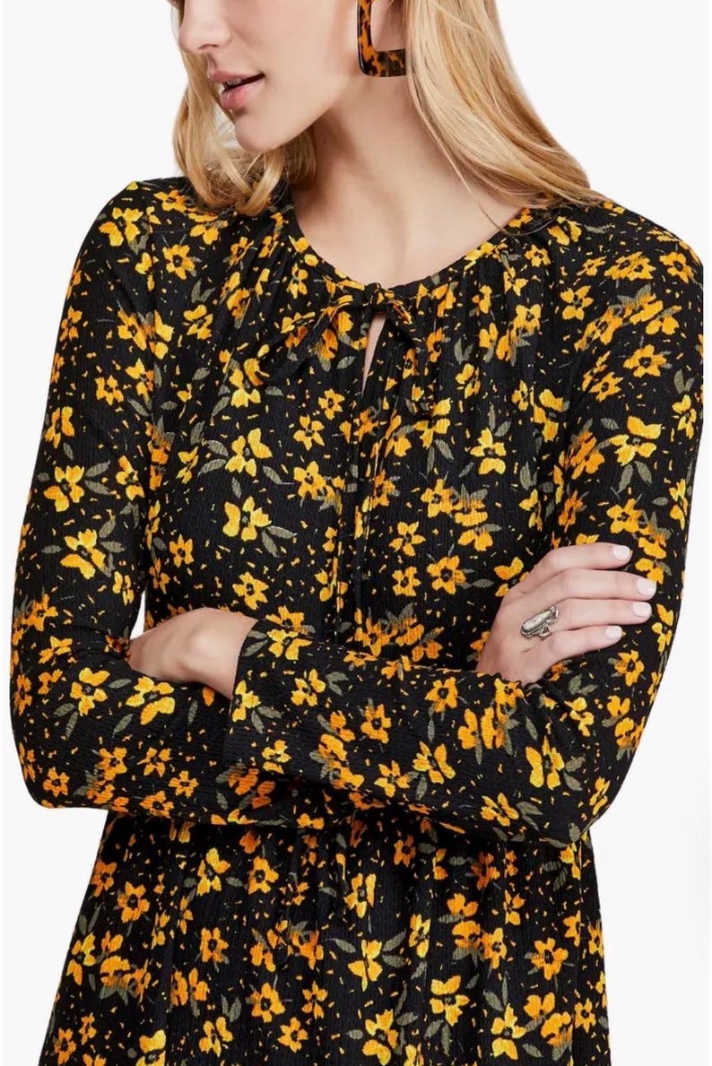 May include: Black long-sleeve dress with a yellow floral pattern. The dress features a tie-neck detail and a fitted waist. The fabric has a textured appearance. The dress is suitable for various occasions.
