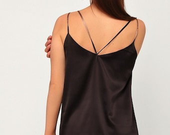 May include: A black satin camisole with thin, criss-cross straps. The top is paired with a satin skirt in a neutral, light brown colour. The image shows the back of the outfit, highlighting the elegant design and fabric.