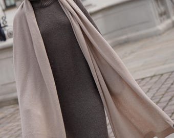 Könnte beinhalten: Ein wadenlanges, langärmeliges Strickkleid in Dunkelbraun mit hohem Rollkragen und geripptem Saum. Das Kleid wird mit einem großen, rechteckigen, hellbeigen Strickschal kombiniert, der über die Schultern gelegt ist und nach vorne fällt.