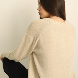 Puede incluir: Un su&eacute;ter beige de manga larga con cuello redondo y mangas ragl&aacute;n. La prenda de punto presenta un cuello, pu&ntilde;os y dobladillo acanalados, mostrando una textura lisa y de color s&oacute;lido en toda la parte posterior y el perfil lateral.