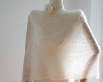 May include: A white knitted shawl with a delicate floral embellishment. The shawl is draped over a white mannequin.
