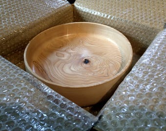 May include: A large, round wooden bowl with a natural wood finish. The bowl is made of light-colored wood with a grain pattern. The bowl is sitting in a box with bubble wrap.