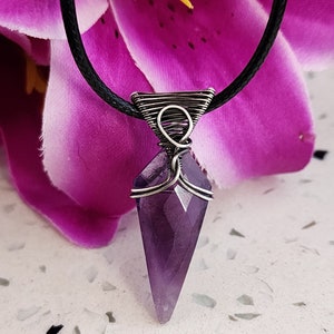 May include: A purple amethyst crystal pendant with a silver wire wrap, hanging from a black cord.