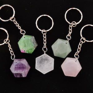 May include: A selection of gemstone keyrings. Each keyring has a faceted, geometric gemstone in different colours, such as green, purple, clear, and pink. The gemstones are attached to silver-coloured key rings with a chain.