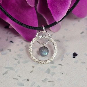 May include: A silver necklace with a round pendant featuring a blue labradorite gemstone. The pendant has an intricate, ornate design.