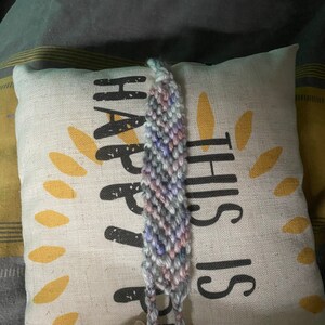 May include: A multi-coloured friendship bracelet with a light blue, pink and grey colour scheme. The bracelet is tied in a knot and is ready to be worn.