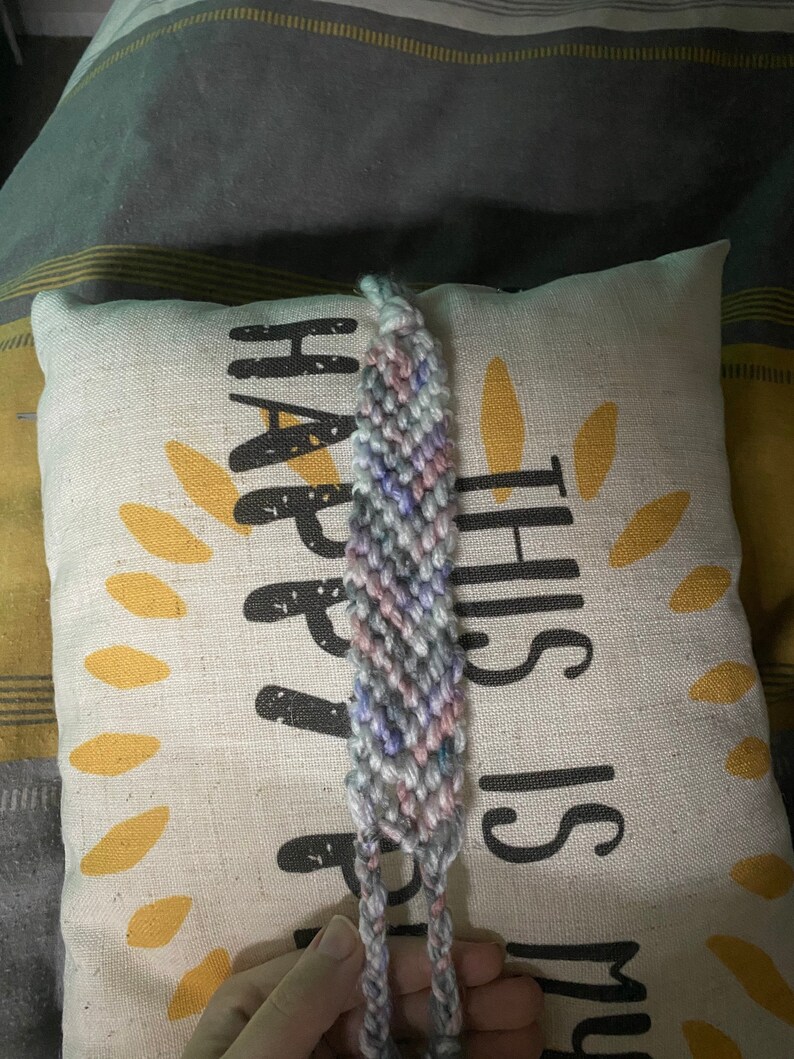 May include: A multi-coloured friendship bracelet with a light blue, pink and grey colour scheme. The bracelet is tied in a knot and is ready to be worn.