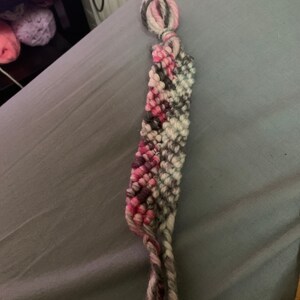 May include: A pink, white and grey friendship bracelet with a knotted end.