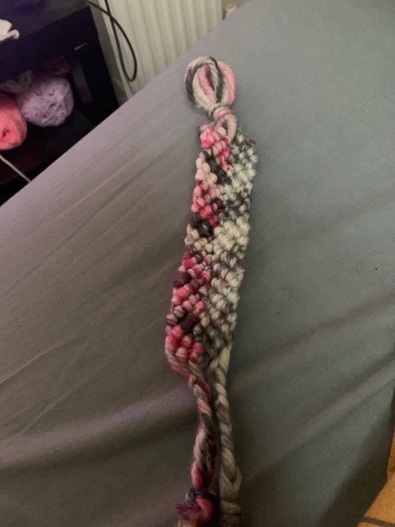 May include: A pink, white and grey friendship bracelet with a knotted end.