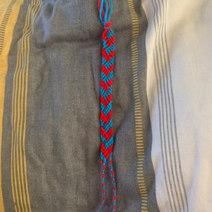 May include: A red and blue friendship bracelet with a chevron pattern.