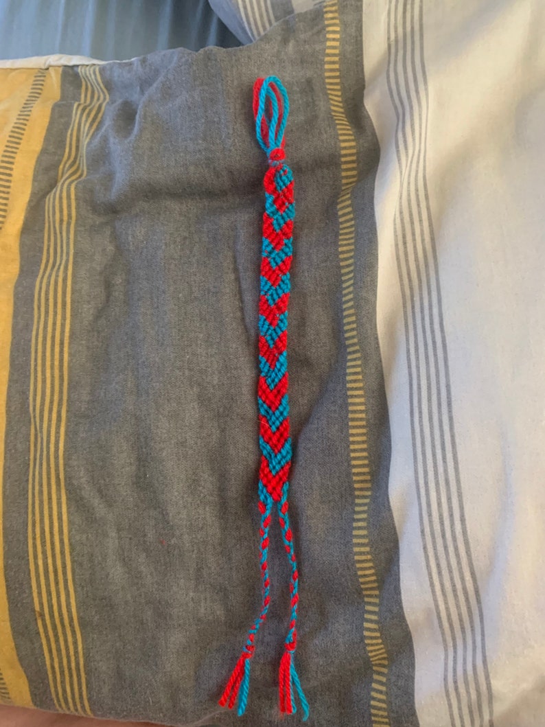 May include: A red and blue friendship bracelet with a chevron pattern.