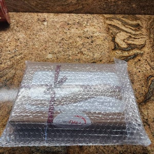 Peut inclure: Une bo&icirc;te rectangulaire en carton brun envelopp&eacute;e dans du papier bulle transparent. La bo&icirc;te est fix&eacute;e par un fin ruban &agrave; motifs rouges et blancs nou&eacute; en boucle. Une &eacute;tiquette ovale blanche avec le texte Debbie Meyer est visible sur le devant.