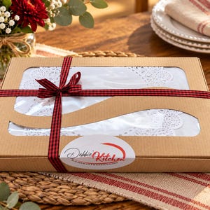 Peut inclure: Une bo&icirc;te cadeau rectangulaire en carton brun avec une fen&ecirc;tre en plastique transparent r&eacute;v&eacute;lant des napperons en dentelle blanche &agrave; l'int&eacute;rieur. La bo&icirc;te est entour&eacute;e d'un ruban &agrave; carreaux rouge et noir nou&eacute; et porte une &eacute;tiquette Debbie's Kitchen.