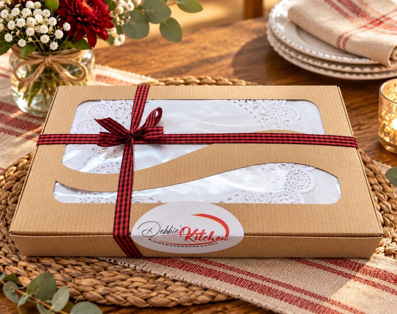 Peut inclure: Une bo&icirc;te cadeau rectangulaire en carton brun avec une fen&ecirc;tre en plastique transparent r&eacute;v&eacute;lant des napperons en dentelle blanche &agrave; l'int&eacute;rieur. La bo&icirc;te est entour&eacute;e d'un ruban &agrave; carreaux rouge et noir nou&eacute; et porte une &eacute;tiquette Debbie's Kitchen.
